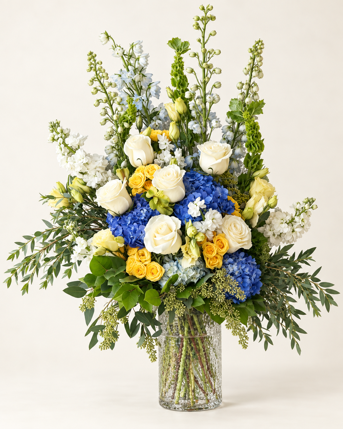 Blue, white and yellow flowers in a glass vase against a warm ivory background