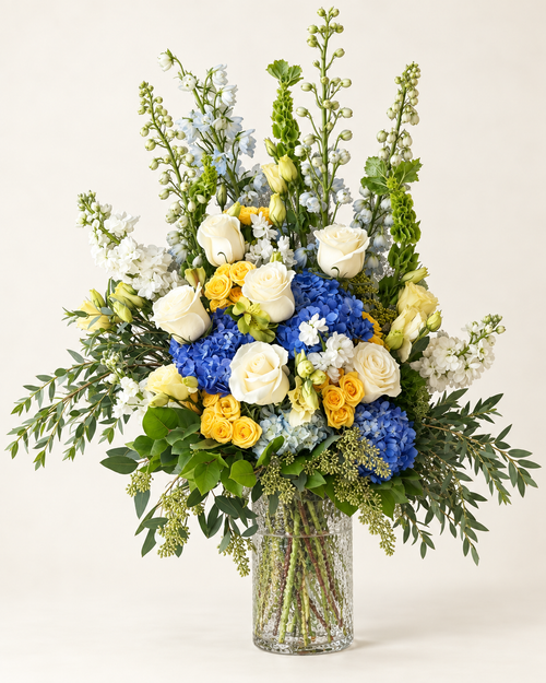 Blue, white and yellow flowers in a glass vase against a warm ivory background