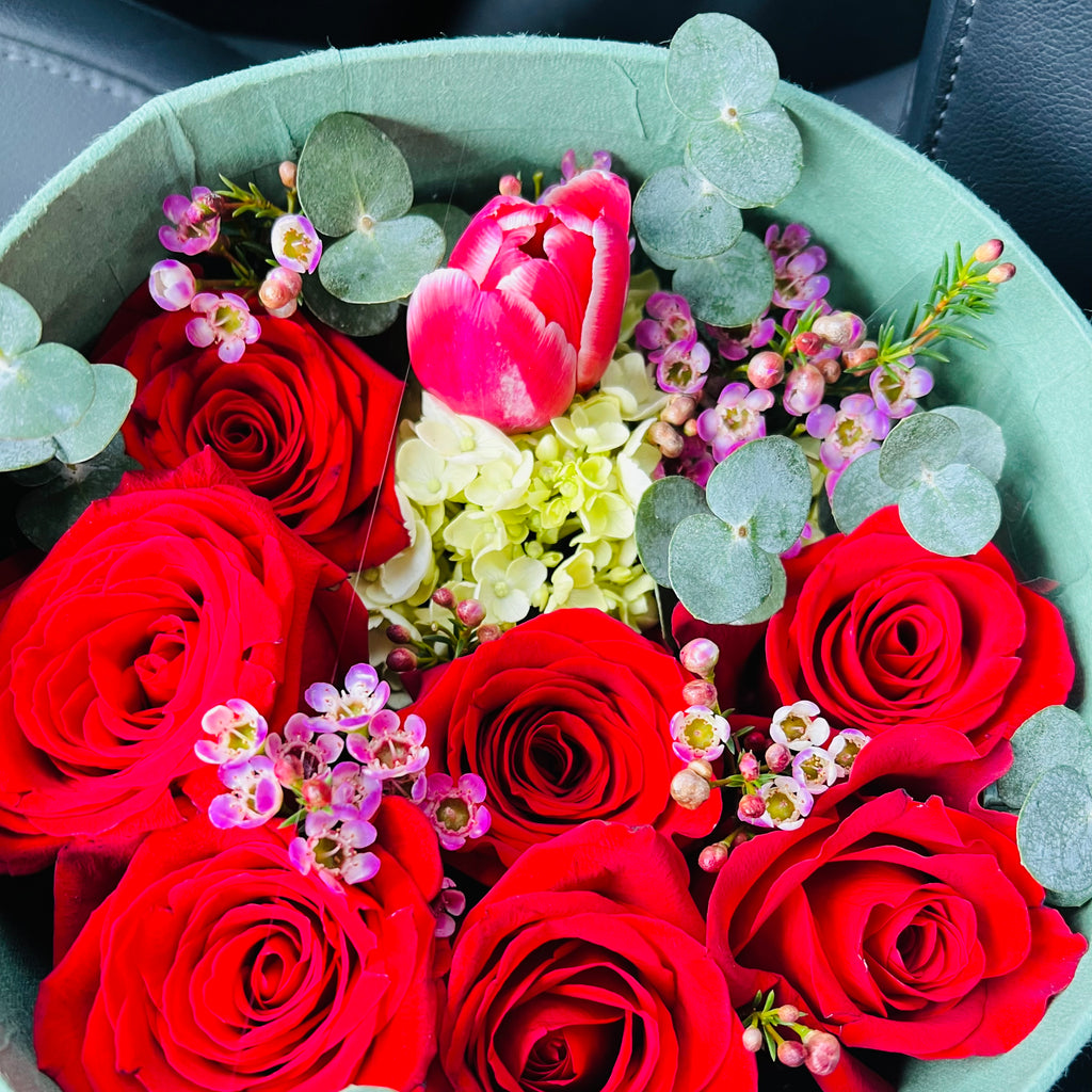 Real close-up photo of the Ruby Romance box with red roses, pink tulip, green hydrangea, waxflower and eucalyptus