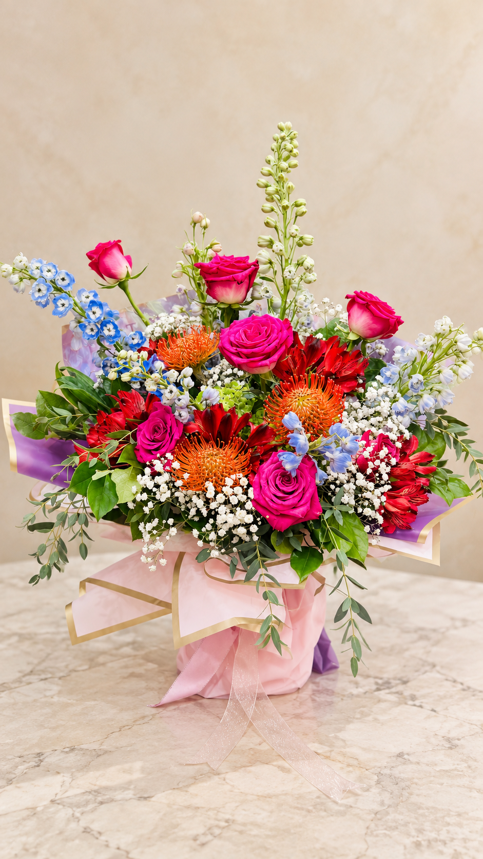 Vivid Celebration Arrangement of magenta roses, blue delphinium and orange pincushion flowers